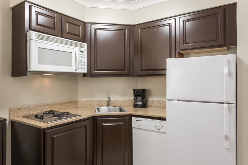 Compact kitchen with dark cabinets, microwave, refrigerator, and sink.