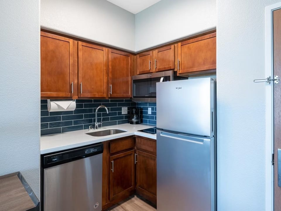 Full kitchen with wood cabinetry, stainless fridge, dishwasher, microwave, and blue tile backsplash