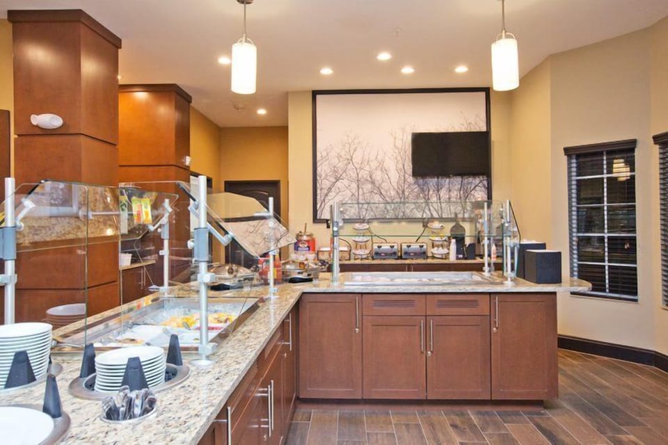 Breakfast buffet counter with covered food displays, plates, and utensils.