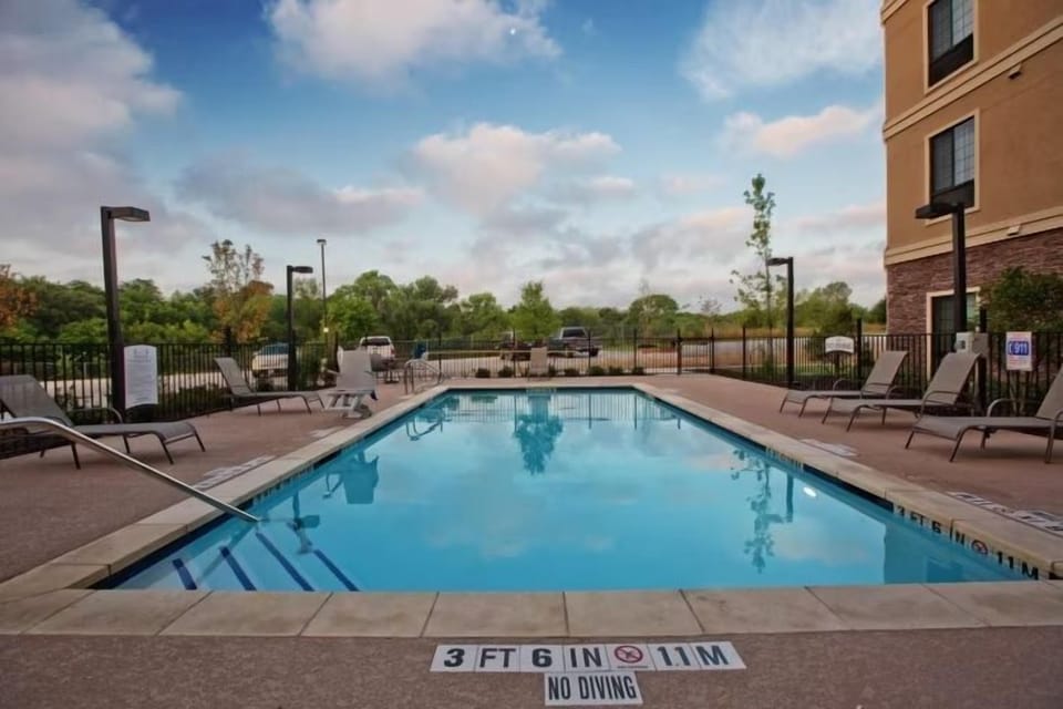 Outdoor swimming pool with lounge chairs and surrounding trees.