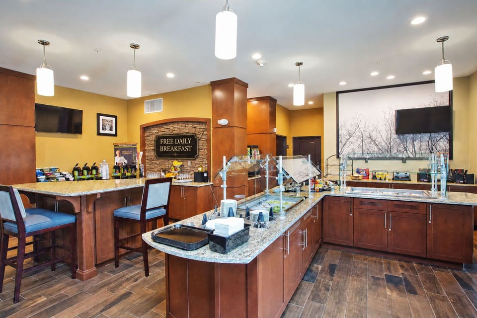 On-site breakfast bar with hot food displays, bar seating, and a mounted TV.