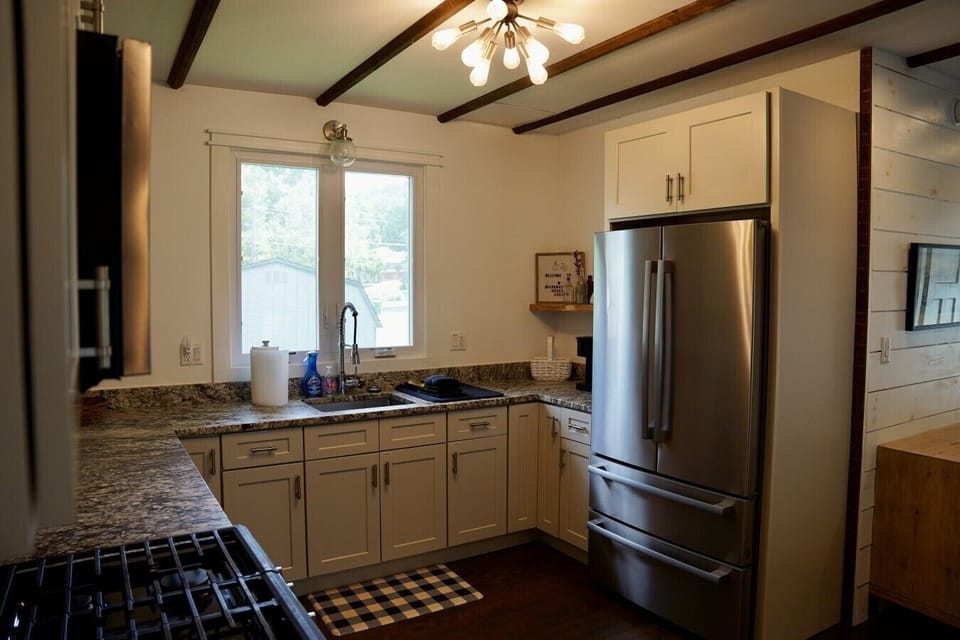 Fully stocked kitchen with granite countertops, cooking supplies for any meal, a stainless steel French door fridge, and gas range. Exposed beams and a sputnik chandelier add warm character, while everything you need is right at your fingertips.