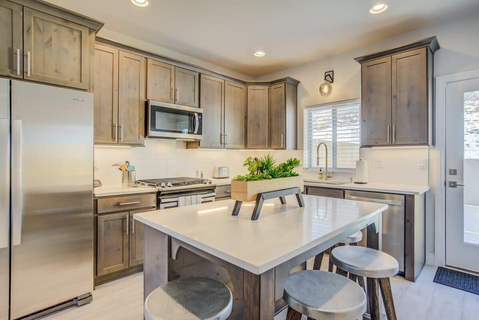 This modern kitchen centers around a bright island with seating, surrounded by warm cabinetry and stainless appliances, perfect for cooking together, casual meals, or lingering morning coffee.