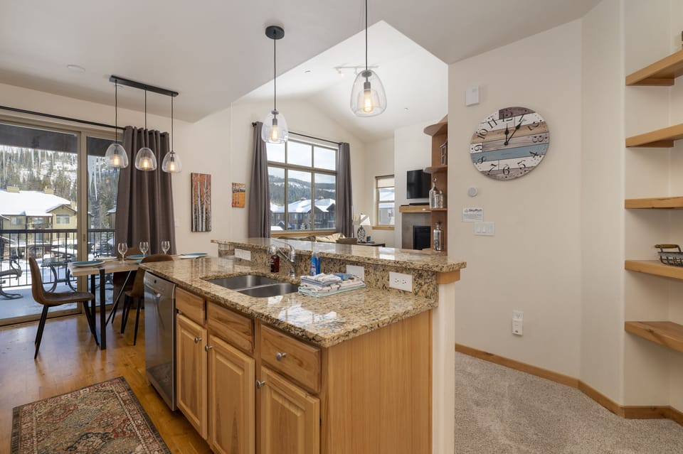 A modern kitchen features granite countertop island, beautiful wooden cabinets, and hanging light fixtures. It is fully stocked with all your cooking needs