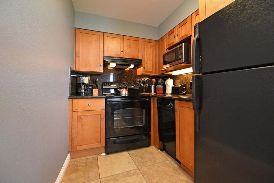Compact kitchen with wooden cabinets, granite counters, and black appliances.