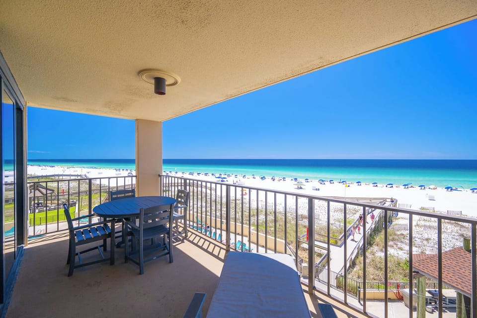 This balcony features a round table with chairs, perfect for enjoying meals while taking in the serene beach view