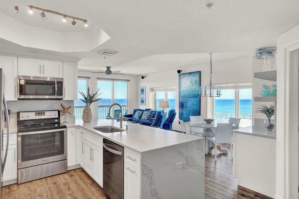 Your fully equipped kitchen flows seamlessly into the living space, where stunning ocean views through floor-to-ceiling windows create the perfect backdrop for cooking and relaxing.