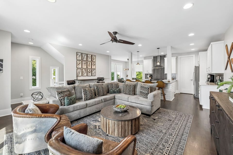 Spacious layout with plush sectional, bar seating, and sleek kitchen all in one view - Modern ceiling fans, warm wood tones, and leather accents enhance the cozy vibe - Perfect for entertaining, relaxing, or enjoying movie nights with friends and family