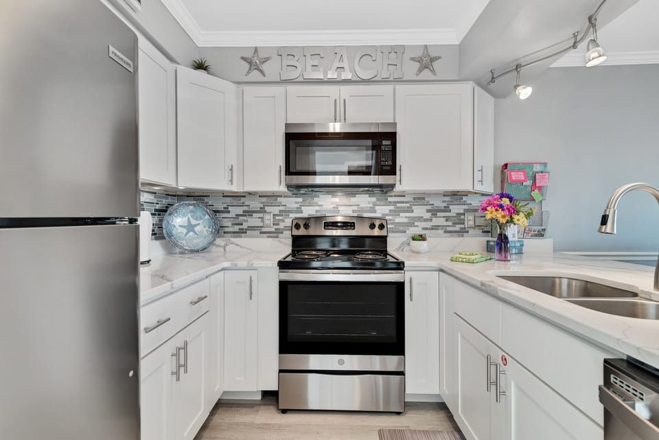 This modern kitchen is fully equipped with sleek white cabinetry, pristine countertops, and a stylish mosaic backsplash, perfect for all your culinary needs.
