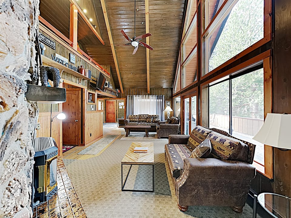Vaulted wood ceilings rise above patterned sofas and a wood coffee table beside floor-to-ceiling windows in the living room.
