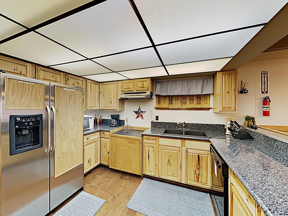 Speckled granite countertops stretch along wood-paneled cabinets with a double-door stainless steel refrigerator.
