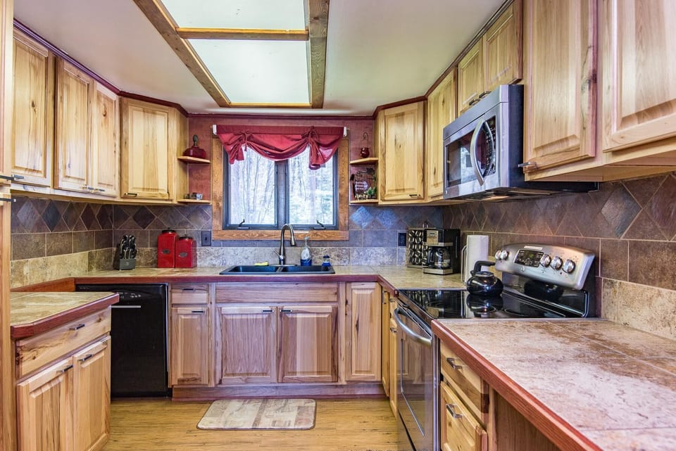 Kitchen with natural wood cabinets, tiled counters and backsplash, skylight, and window over black sink.