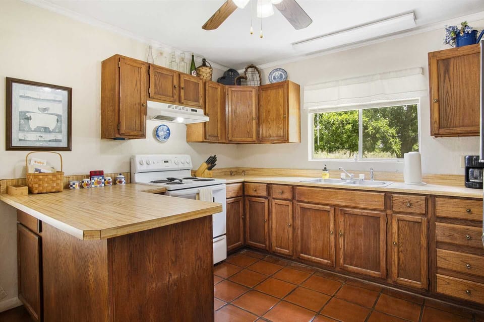Fully equipped country kitchen with warm wood cabinets and a view of the lush outdoors.