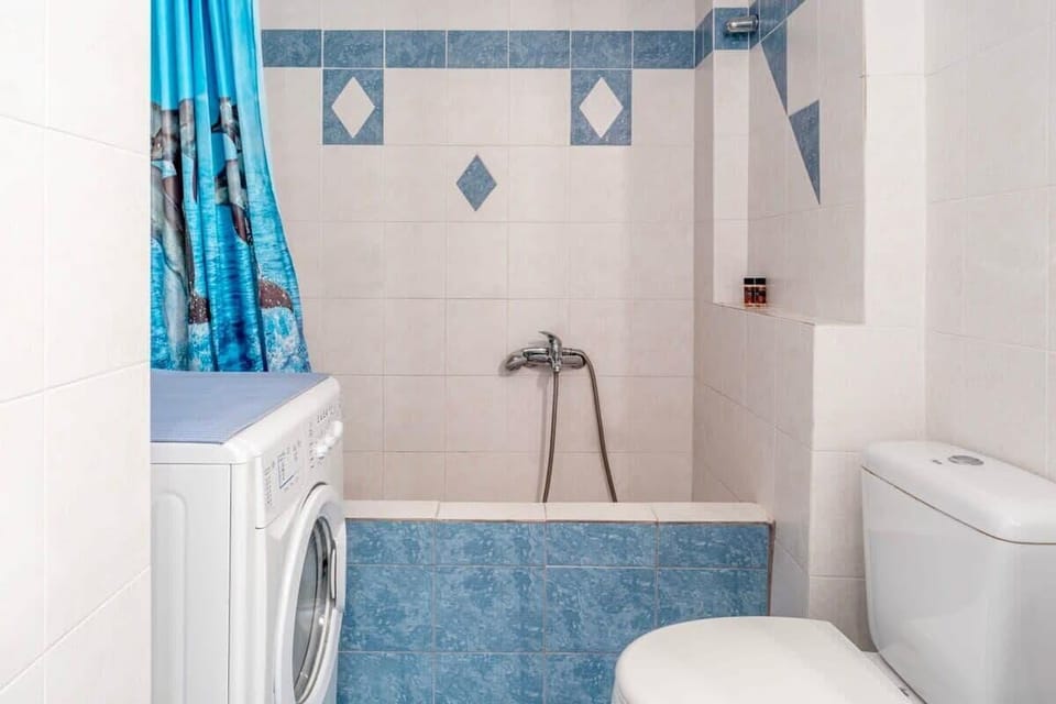 Blue and White Bathroom with Shower
A bright bathroom with a blue shower curtain, white toilet and sink, and tile floors.