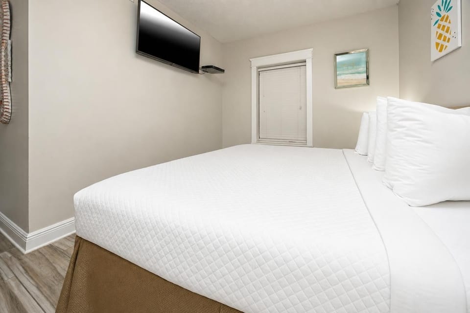 A cozy guest bedroom features a plush king bed with crisp linens, a mounted TV, and cheerful beach artwork on the walls