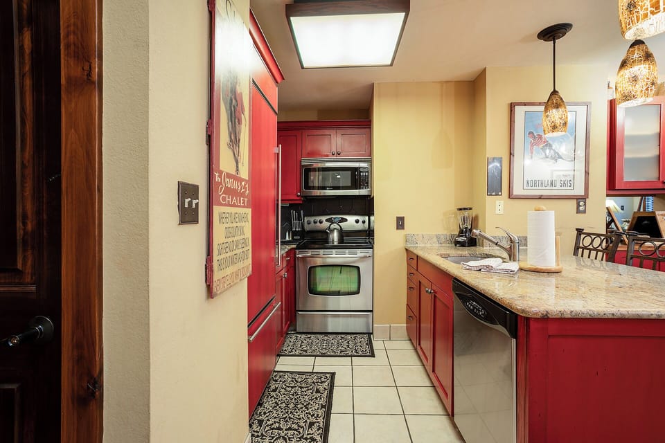 Your fully equipped kitchen features warm red cabinets, granite countertops, and modern appliances for preparing memorable meals during your stay.