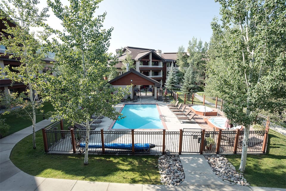 Property's outdoor pool area surrounded by mature trees and mountain lodge-style buildings, creating a peaceful resort atmosphere.