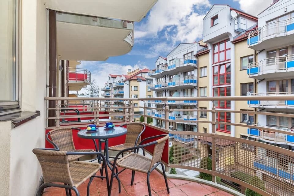 This balcony showcases a charming outdoor space with a small round table and two red chairs. It offers views of neighboring apartment buildings and a green courtyard below.