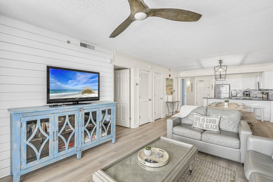 Relax in this bright coastal living room where beach vibes meet comfort—your perfect retreat with entertainment center and open kitchen nearby.