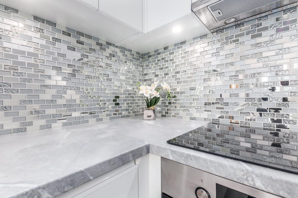 A beautiful kitchen with reflective silver mosaic tiles as a backsplash, modern white cabinetry, and state-of-the-art appliances, perfect for stylish cooking.