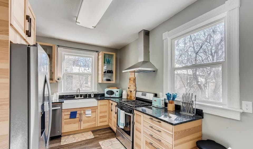 - Sleek and spacious kitchen with stainless steel appliances, range hood, and farmhouse sink
- Light wood cabinetry and black granite countertops offer a clean modern look
- Large windows and wood floors add brightness and warmth to the space