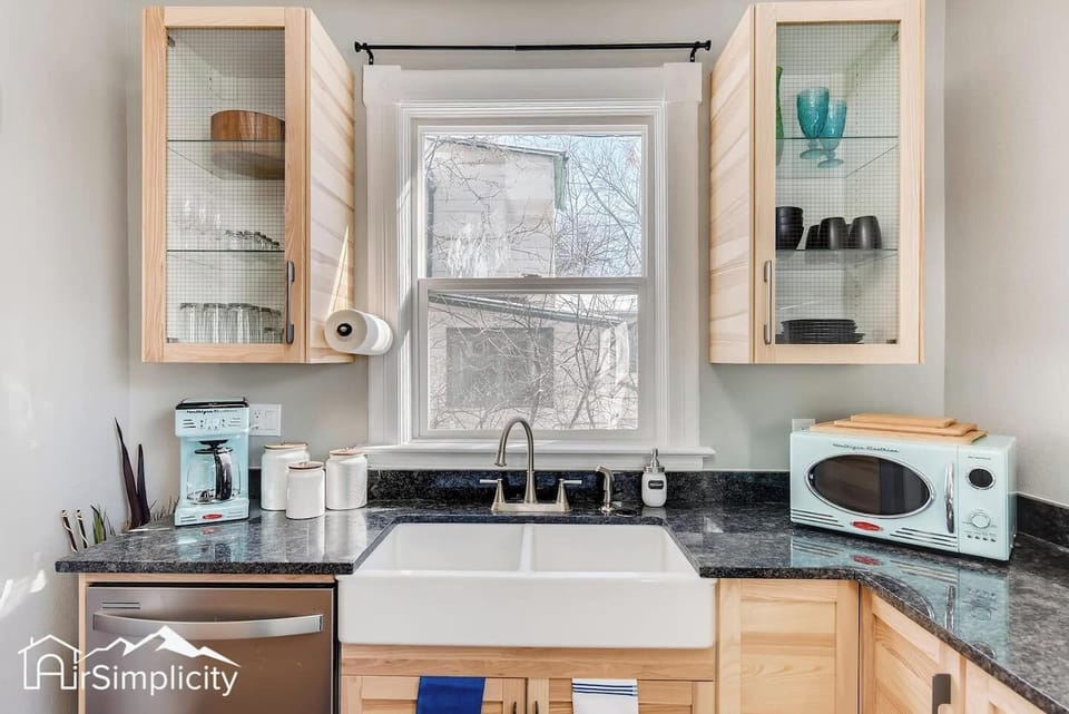 - Farmhouse sink beneath a bright window pairs beautifully with wood cabinetry and granite counters
- Glass front cabinets and open shelves display stylish dishware and mugs
- Includes microwave, coffee maker, toaster, and essential kitchen tools