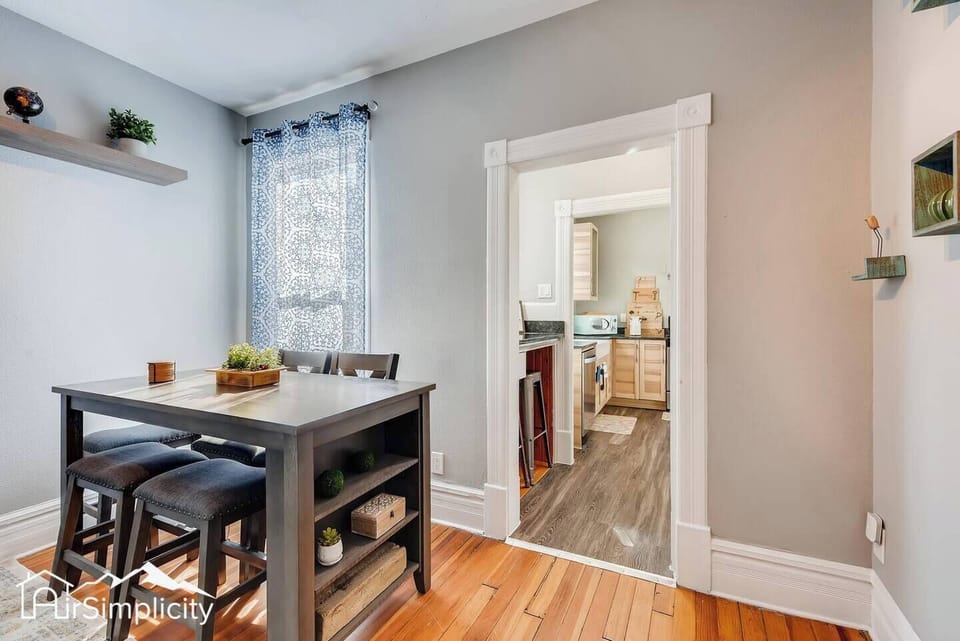 - Compact dining space features a tall table with bench and chairs for group meals
- Stylish shelving and a patterned curtain add warmth to the neutral palette
- Easy access to the kitchen through a classic framed doorway
