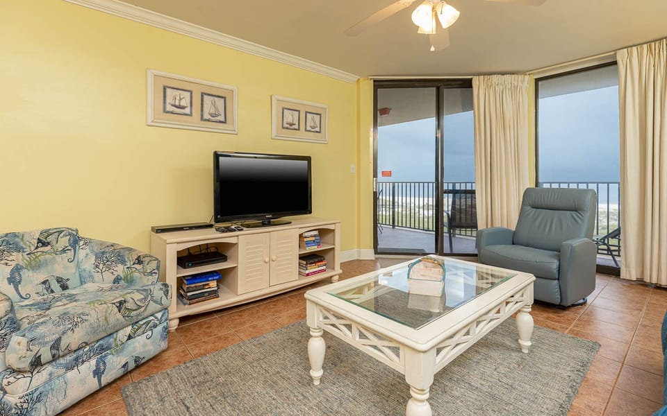 Cozy living area features a patterned loveseat, a glass coffee table, and a TV, with sliding doors leading to the balcony