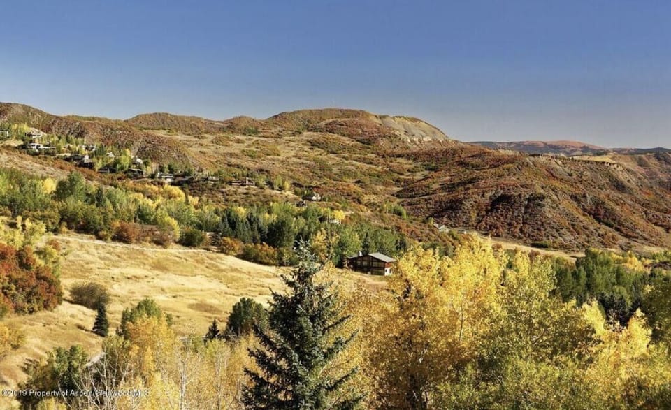 A scenic view of a rural landscape during autumn, featuring rolling hills, colorful foliage, scattered houses, and a clear blue sky.