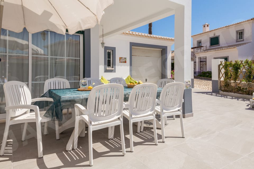 Spacious outdoor dining terrace at Jardim Secreto villa in Carvoeiro, with a large table and white chairs shaded by a parasol, perfect for alfresco meals in the Algarve sunshine