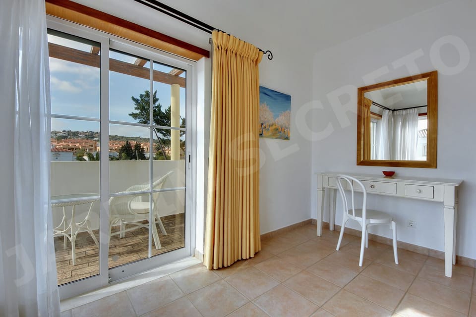 Bedroom at Jardim Secreto villa in Carvoeiro with balcony doors opening onto a private terrace with views, golden curtains, a dressing table with wooden mirror, and a coastal painting on the wall
