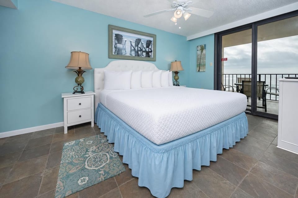 Turquoise walls complement the master suite, while sliding glass doors reveal the balcony with a serene beach front view