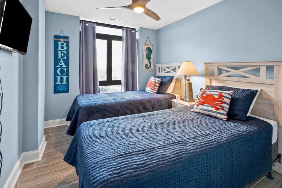 Two beds under a ceiling fan with seashell wall decor at Sedgefield North 404, a Cherry Grove vacation rental