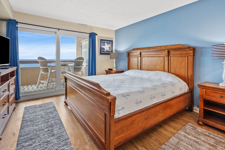 Bedroom with a blue accent wall and sliding doors to an ocean-view balcony at Sea Pointe 802, Cherry Grove