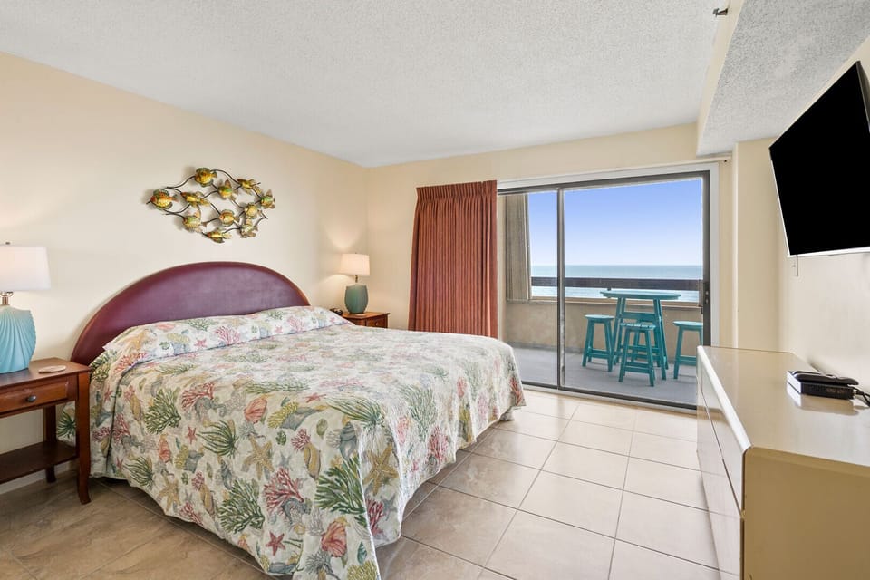 Bedroom with a floral bedspread and a sliding door to the balcony at Sea Pointe 708, Cherry Grove