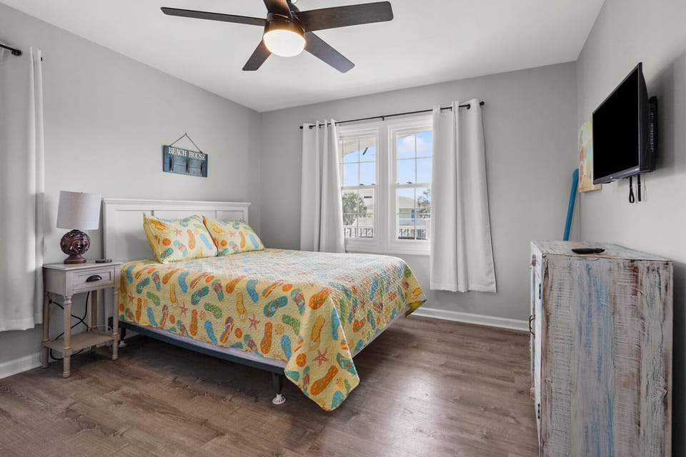 Beach-themed bedspread, a dresser and a TV in a light bedroom at Pelican's Perch in Cherry Grove