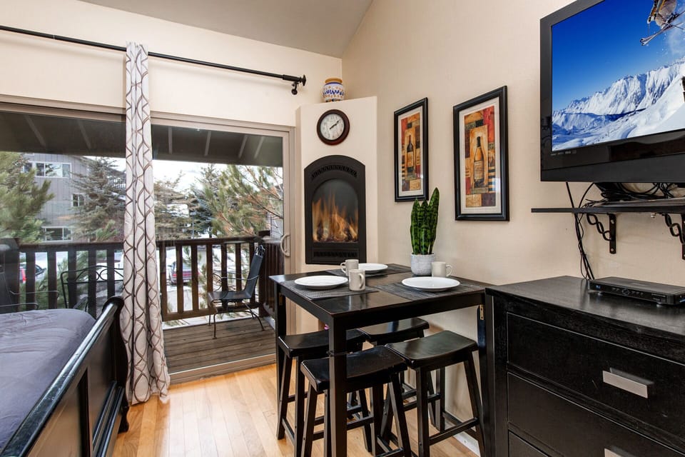 Cozy dining nook with fireplace and balcony access invites you to enjoy meals with stunning mountain views, perfect for après-ski relaxation.