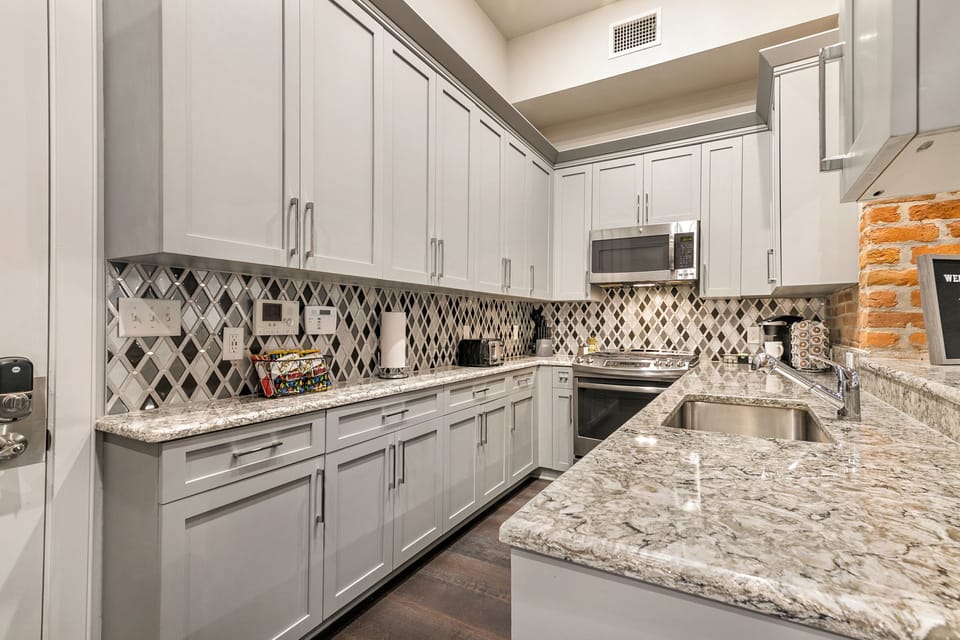 Galley-style, fully equipped kitchen with an open flow to the living/dining area. Stocked with essentials from mixing bowls to wine glasses, featuring stainless steel appliances, a gas range, stone countertops, and a luxury tile backsplash!