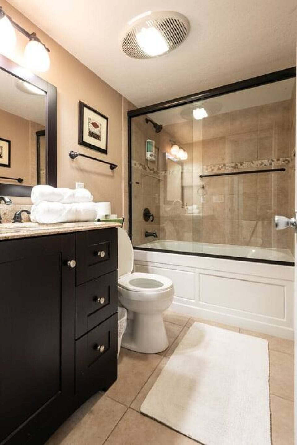 The primary bathroom pairs a dark vanity with a glass-enclosed tub and shower for a practical private retreat.