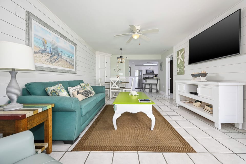 Living area features a turquoise sofa with colorful pillows, a unique green coffee table, and a view toward the dining space