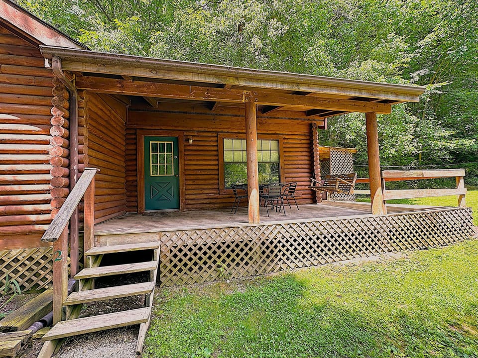 Covered porch with wooden lattice skirting, metal outdoor dining set, and a wooden porch swing surrounded by trees.