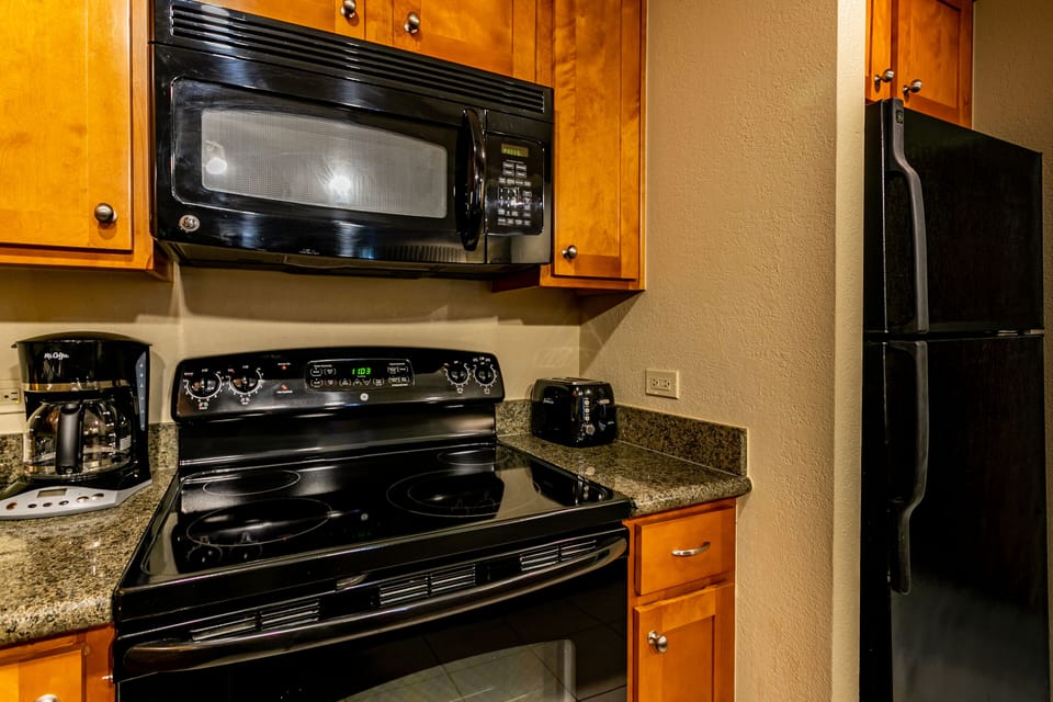 Your fully equipped kitchen features modern black appliances, granite counters, and warm wood cabinetry—perfect for preparing meals during your stay.
