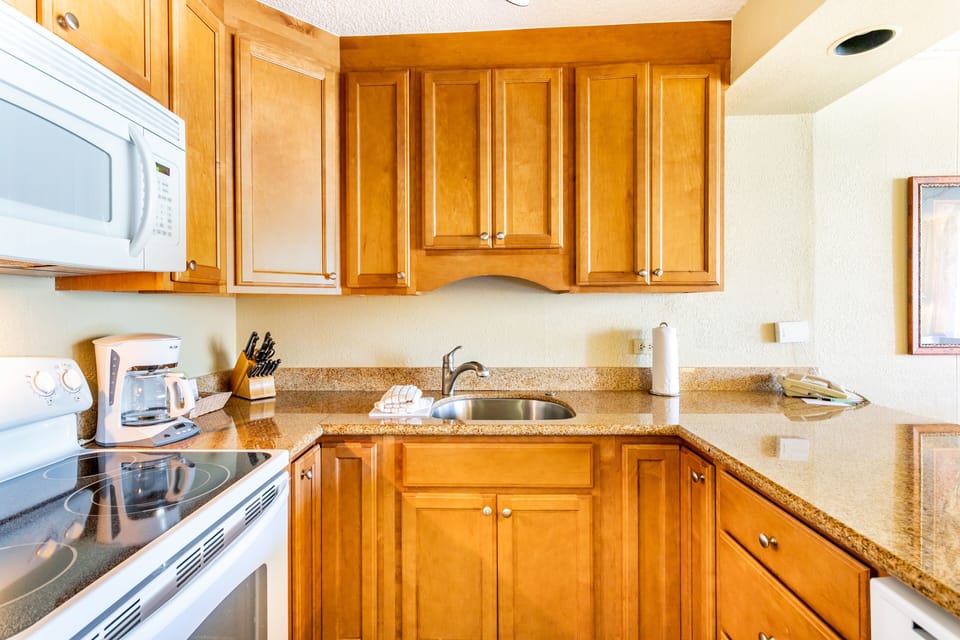Your fully equipped kitchen features warm wood cabinets, granite countertops, and modern appliances including a microwave, stove, and coffee maker—perfect for preparing your favorite meals during your stay.