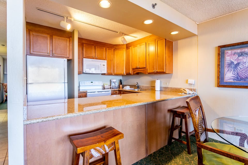 Step into your fully equipped kitchen featuring warm wood cabinetry, granite countertops, modern appliances, and a breakfast bar perfect for morning coffee or quick meals.