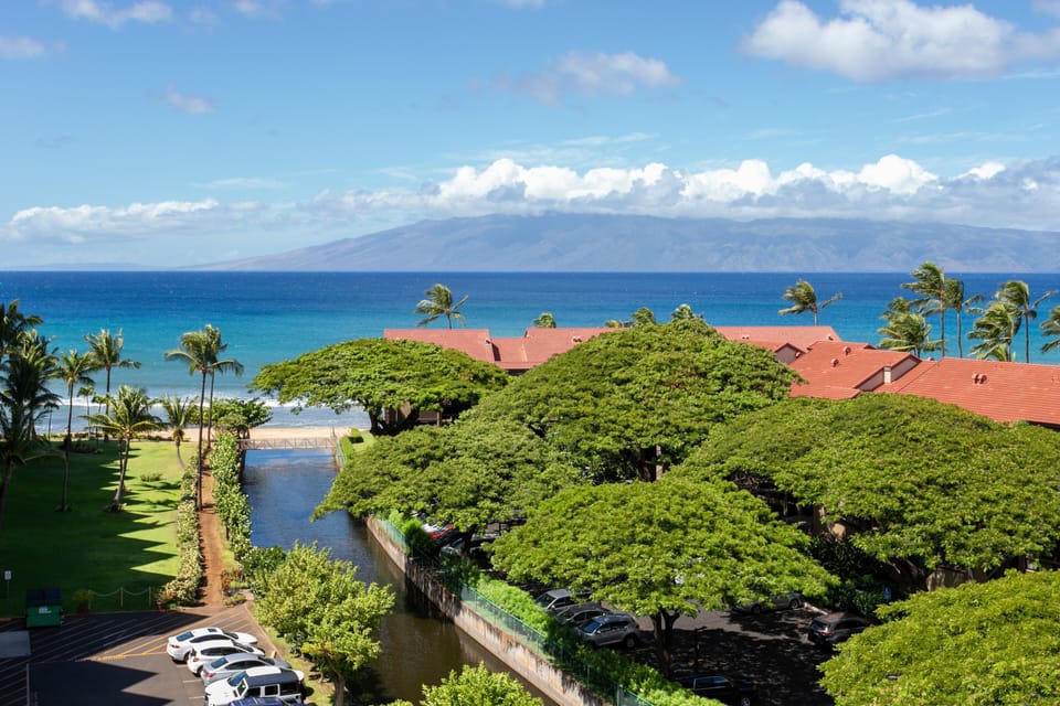 A beachfront property framed by vibrant greenery, overlooking turquoise ocean waters and distant island mountains—a serene tropical escape.