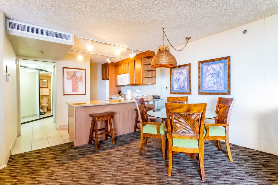 Your open-concept space blends a fully equipped kitchen with a welcoming dining area featuring warm wood furnishings and tropical accents—perfect for sharing memorable meals together.