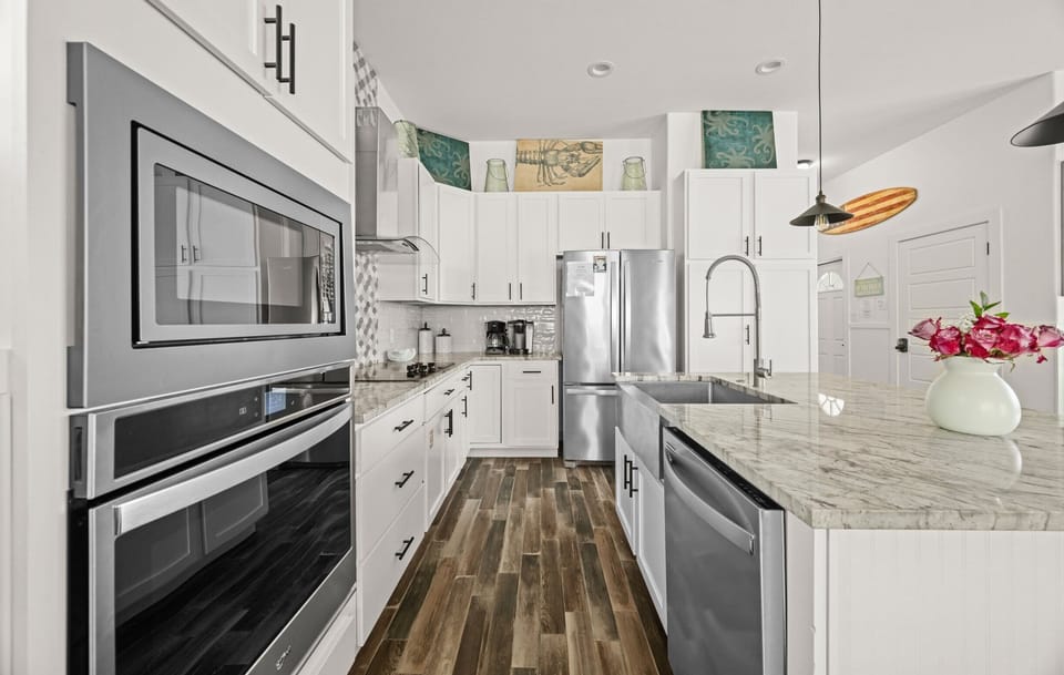 Kitchen — White Cabinets, Marble Counter, Stainless Wall Oven & Microwave, Sea Creature Art & Surfboard Decor