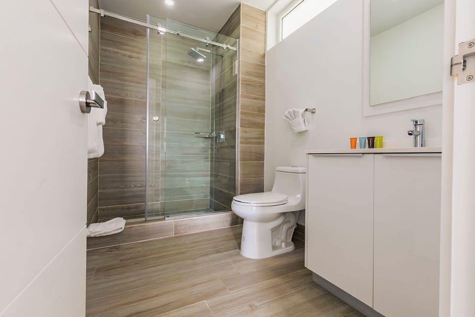 Step into your modern bathroom with a glass-enclosed rainfall shower, wood-look tile, and a floating vanity designed for your comfort and convenience.