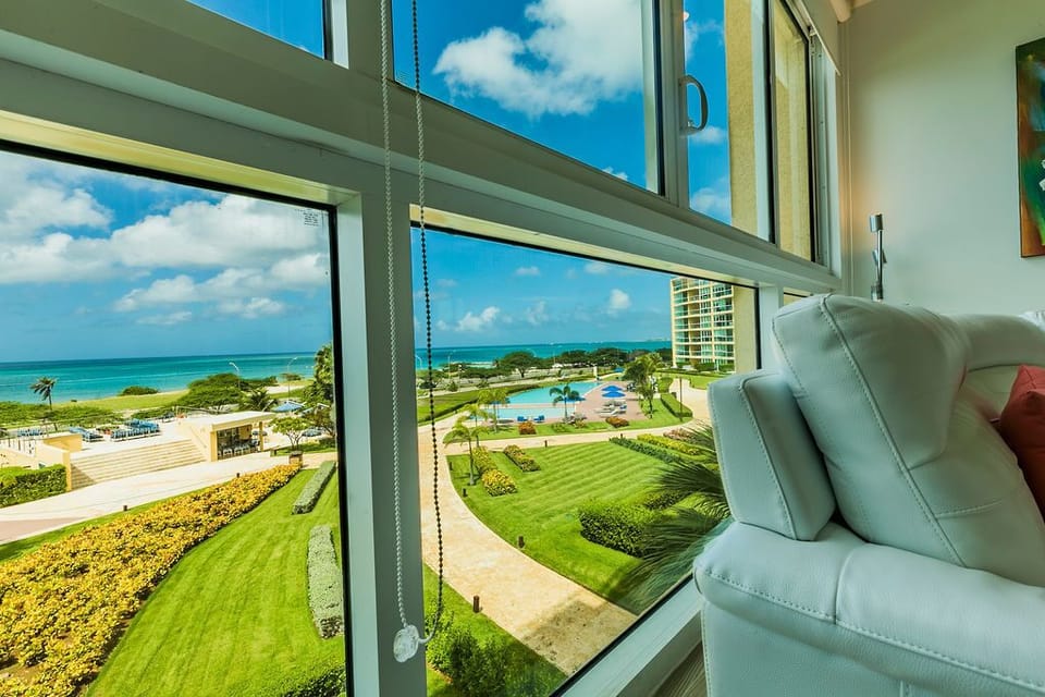 Settle into your cozy living space with sweeping views of manicured gardens, the sparkling pool, and turquoise ocean beyond—perfect for morning coffee or sunset relaxation.