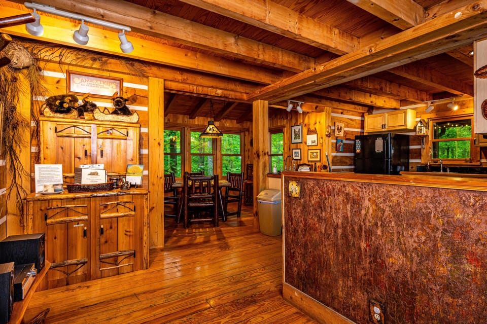 Rustic kitchen and dining area with log beams, wood floors, black appliances, and a textured stone kitchen island.